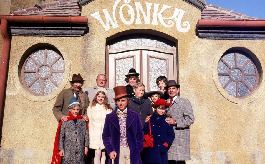 Willy Wonka with the children and their parents posing in front of the Wonka factory entrance 