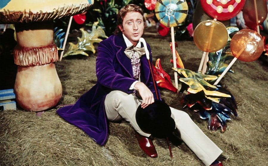 Gene Wilder as Willy Wonka sitting in front of fake lollipops 