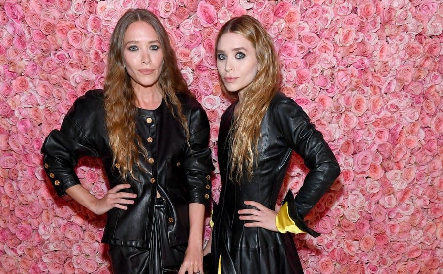 Mary Kate and Ashley Olsen pose on the red carpet in front of a wall of pink roses 