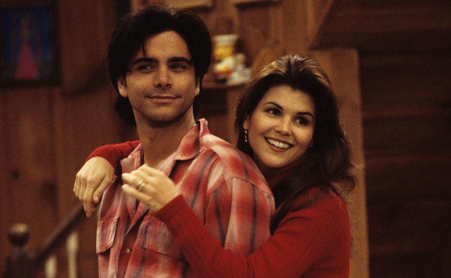 John Stamos with Lori Loughlin going to hug him from behind on the set of Full House 