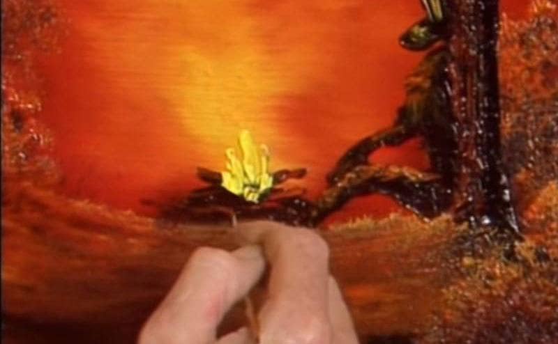 A close-up shot of ross painting a small fire with his paintbrush. 