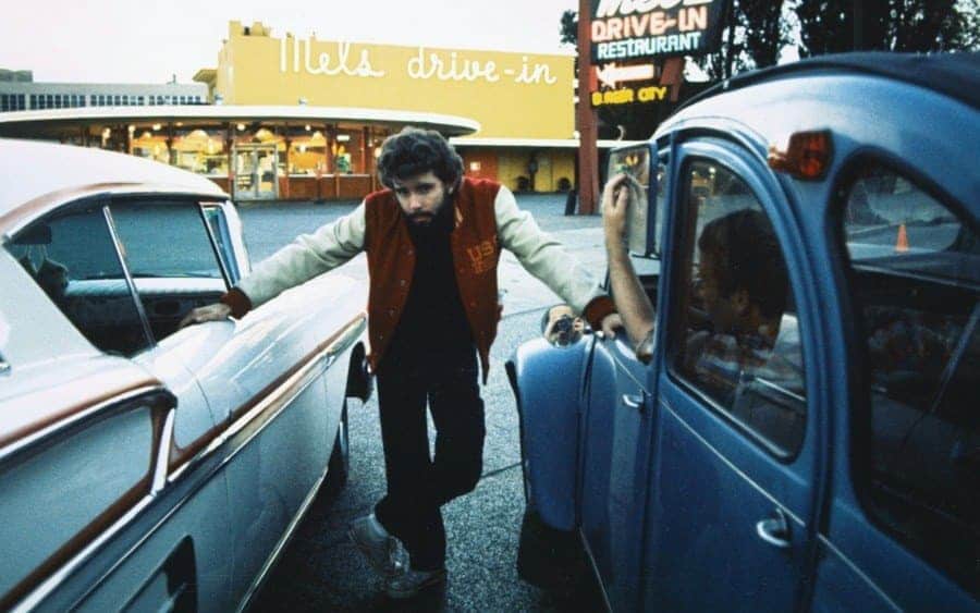 George Lucas, posing between two cars 