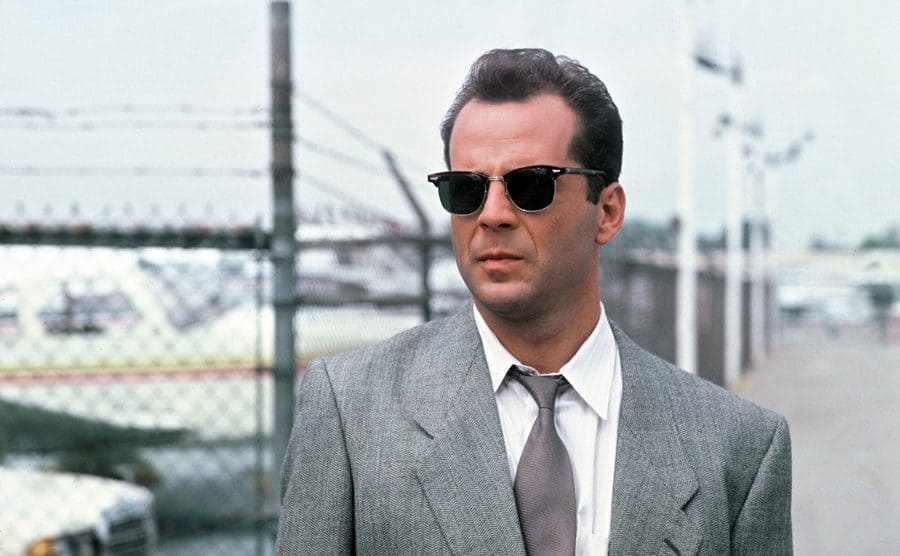 Bruce Willis is looking off into the distance with sunglasses.