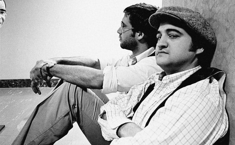 Chevy Chase and John Belushi sitting against a wall backstage on the set of SNL 