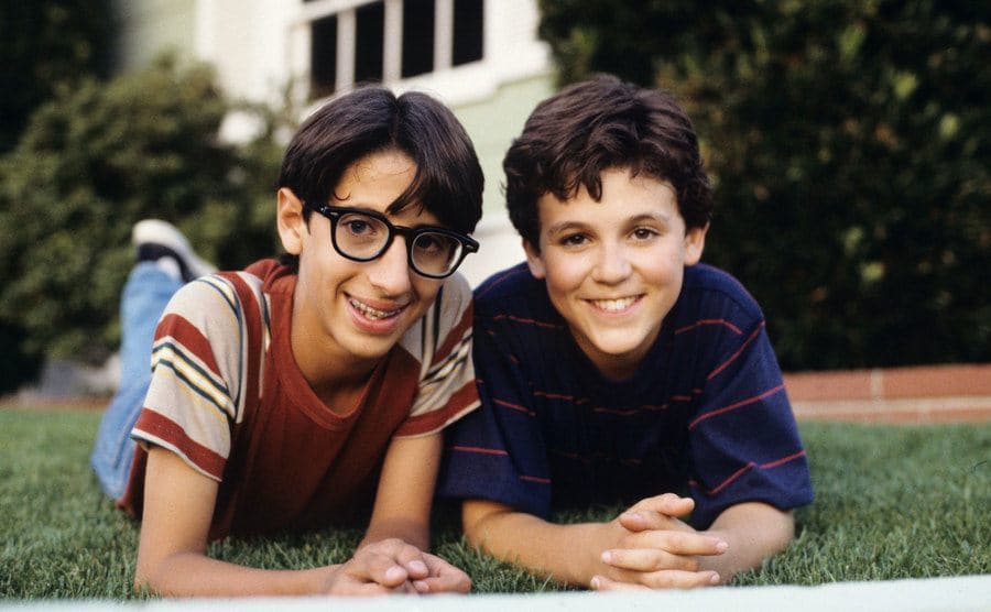 Fred Savage and Josh Saviano are smiling as they relax on the grass. 