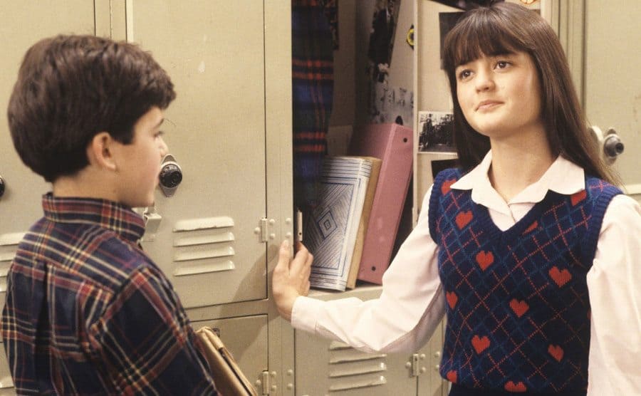 Winnie and Kevin have a conversation while standing next to Winnie’s locker at school. 