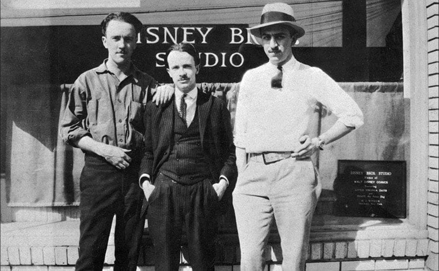 Walt Disney and two other men stand in front of the studio doors. 