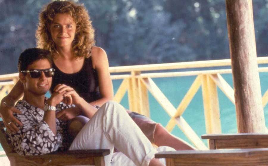 Tom Cruise and Elizabeth Shue are sitting hugging and holding hands next to the sea.