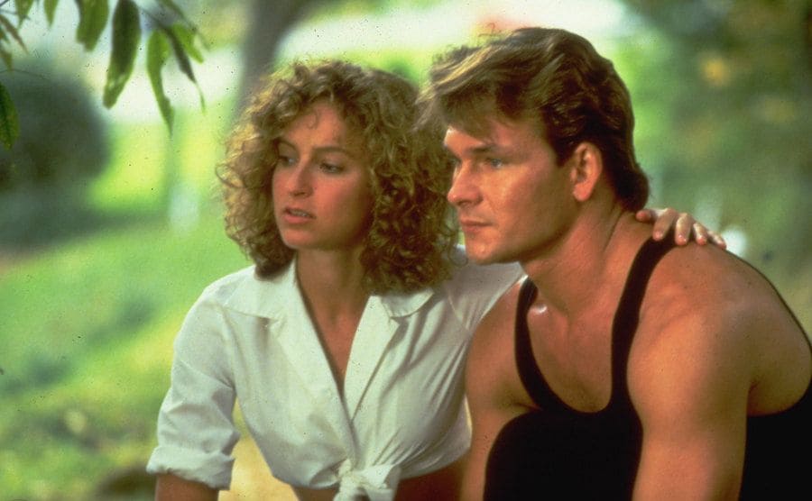 Jennifer Grey is sitting next to Patrick Swayze in a summery nature.