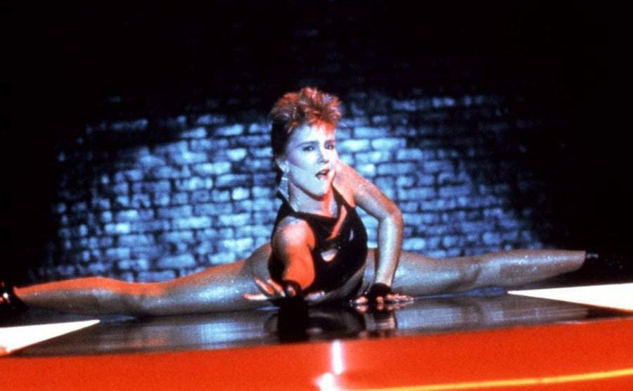 Cynthia Rhodes is doing a legs split on stage in a scene of the movie Flashdance. 