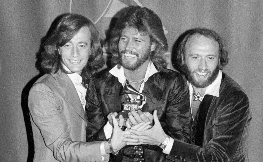 The Bee Gees, brothers Robin, Barry, and Maurice Gibb, hold their Grammy for their Album of the Year Award.