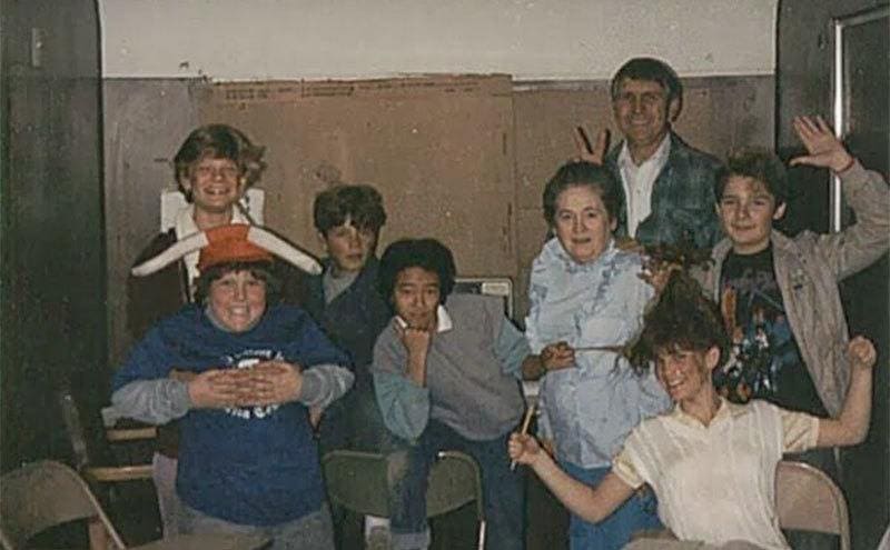 The cast of The Goonies are posing for a silly group photo behind the scenes. 