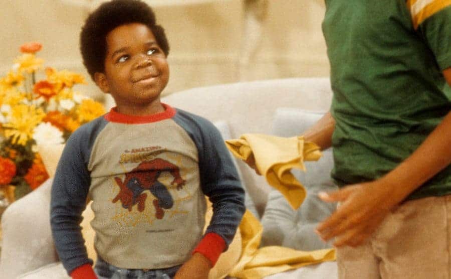 A 10-year-old Gary Coleman is standing in a living room filled with flowers and tiny tea cups.