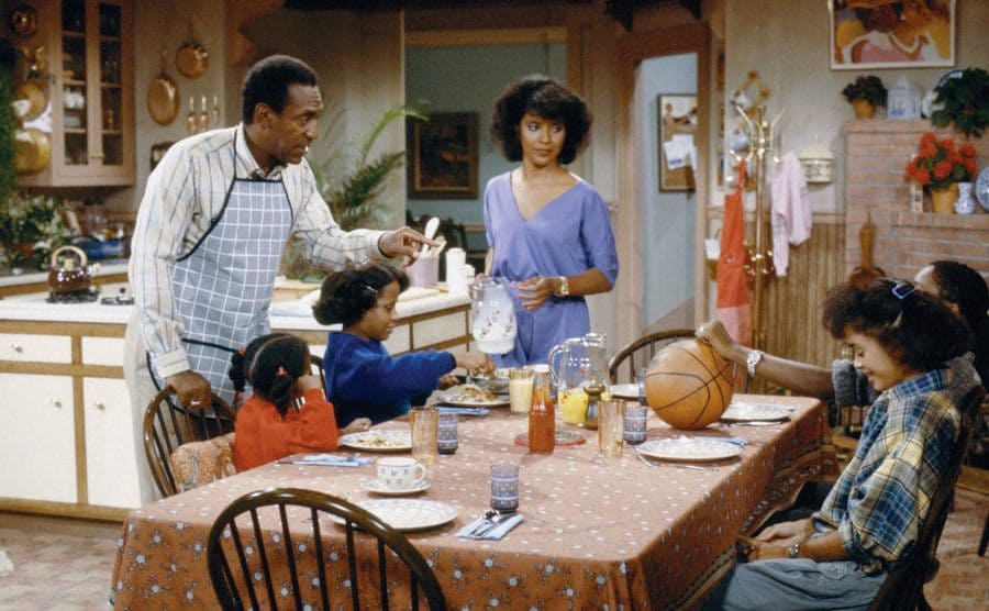 Cosby talking to his four kids who are sitting at the kitchen table. 