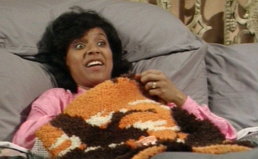 Phylicia Rashad lying in bed with multiple covers hiding her baby bump. 