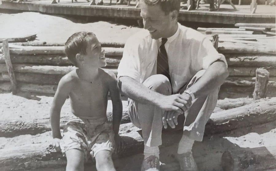 Young Chevy Chase as a child, sits and smiles at his father sitting next to him. 