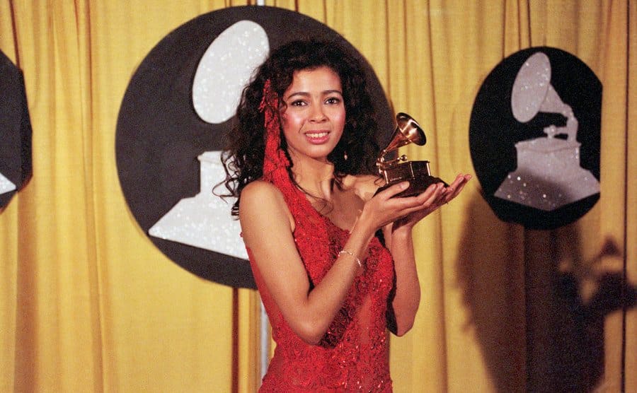 Irene Cara is posing and holding her award for the song What a Feeling from the movie Flashdance.