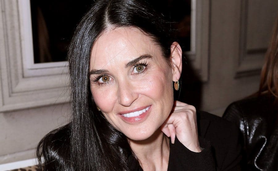 Demi Moore is sitting and smiling for the press while attending a Monot show at Paris Fashion Week, circa 2021.