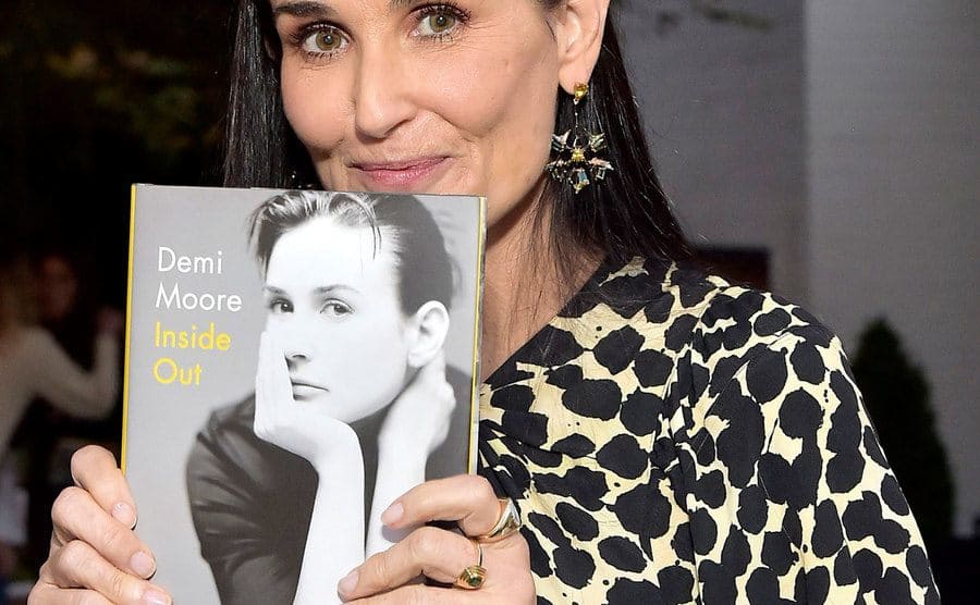 Demi Moore is posing for the press holding her book ‘Inside Out’ at a book party.