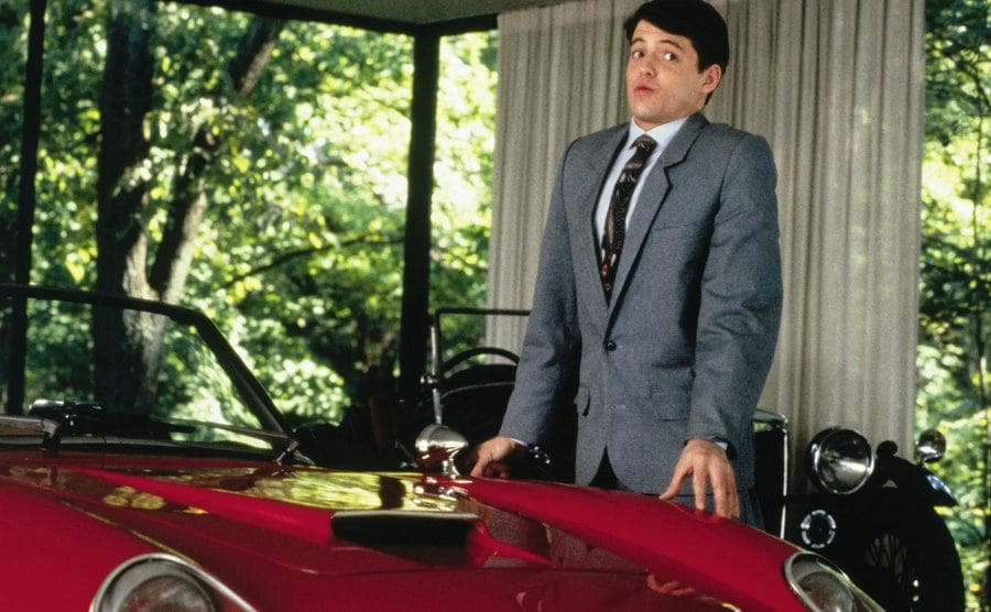 Broderick, as Bueller, stands over the iconic Ferrari. 