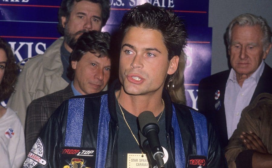 Rob Lowe speaks on stage in front of a crowd. 