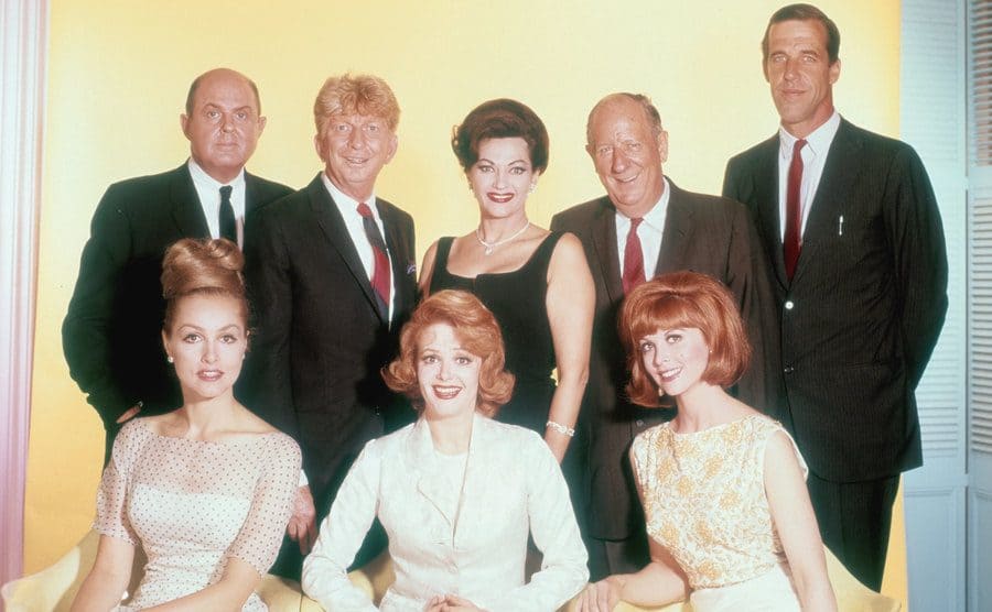 Fred Gwynne is posing in a studio portrait of CBS main television stars among John McGiver, Sterling Holloway, Yvonne De Carlo, Paul Ford, Cara Williams, and Tina Louise. 