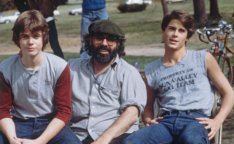 C.Thomas Howell, Francis Coppola, and Rob Lowe are sitting on a bench at the set of The Outsiders.