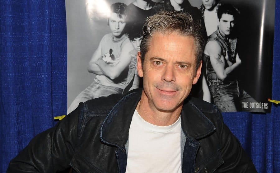 C. Thomas Howell is posing before 'The Outsiders' poste.