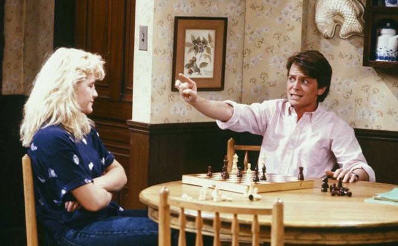 Tina Yothers and Michael J. Fox are playing chess in a scene from the tv show. 