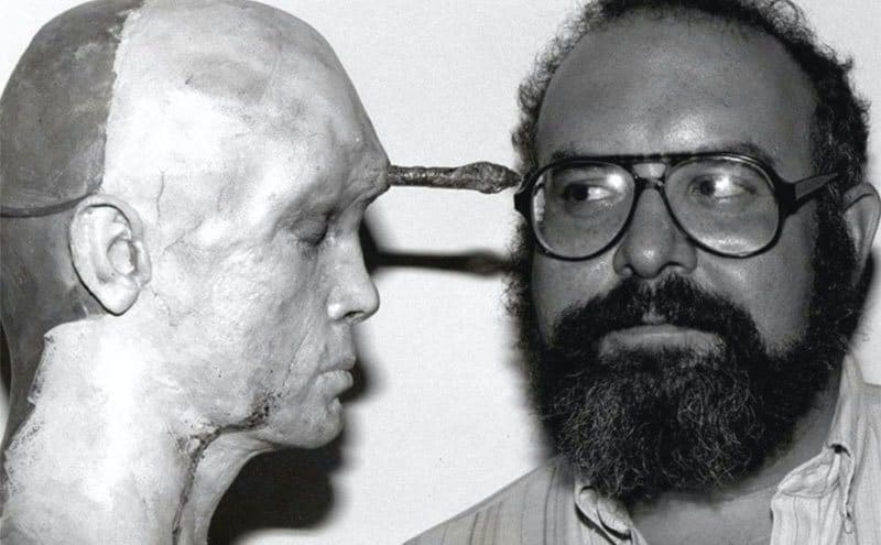 Stuart Gordon poses next to a doll behind the scenes of Re-Animator.