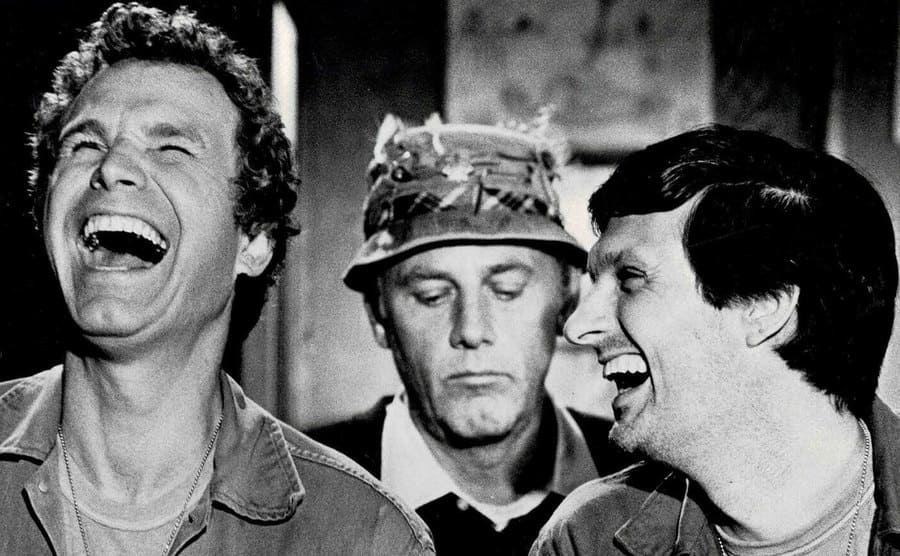 Wayne Rogers, McLean Stevenson, and Alan Alda break into laughter in a scene.