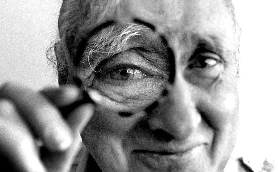  Spike Milligan holds a magnifying glass up to his eye. 