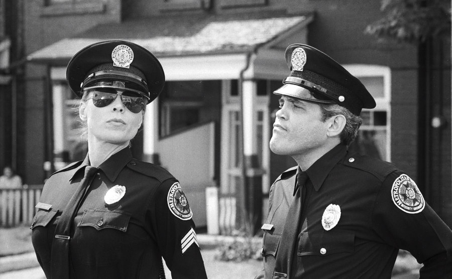 Leslie Easterbrook and G.W. Bailey standing side by side in police uniforms. 