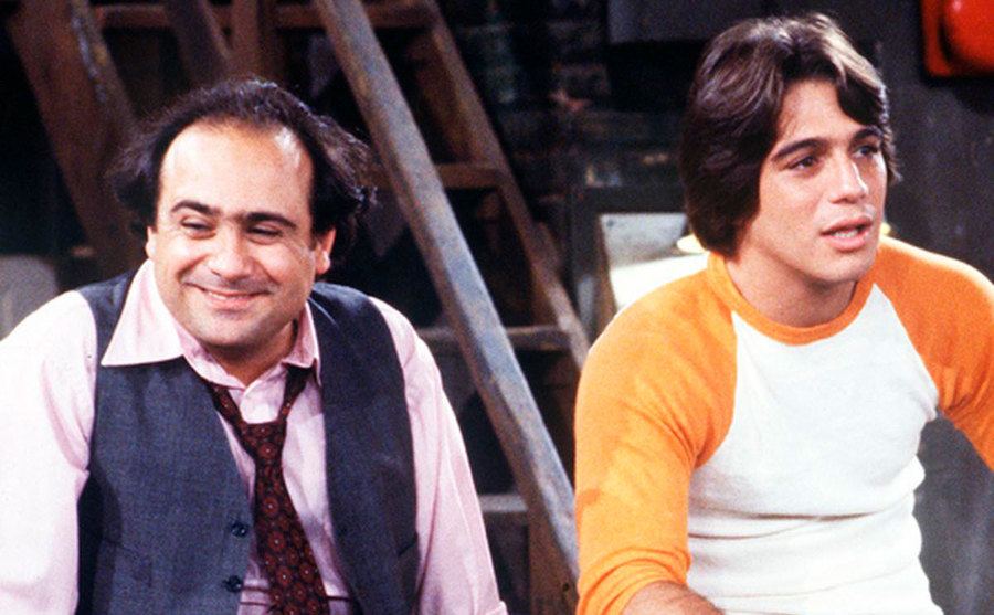 Tony Danza and Danny DeVito sit on the hood of a cab in a still from Taxi. 