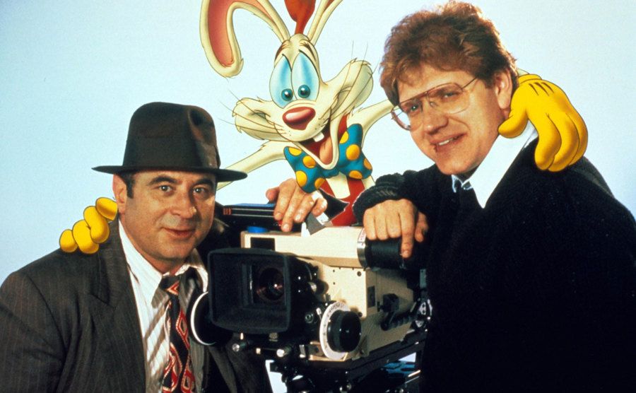 Bob Hoskins, Robert Zemeckis, and Roger Rabbit pose next to a film camera. 