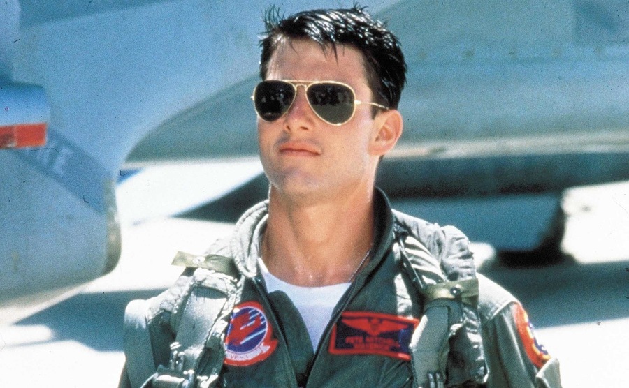 Tom Cruise walks across the tarmac with his aviator sunglasses in a scene from Top Gun. 
