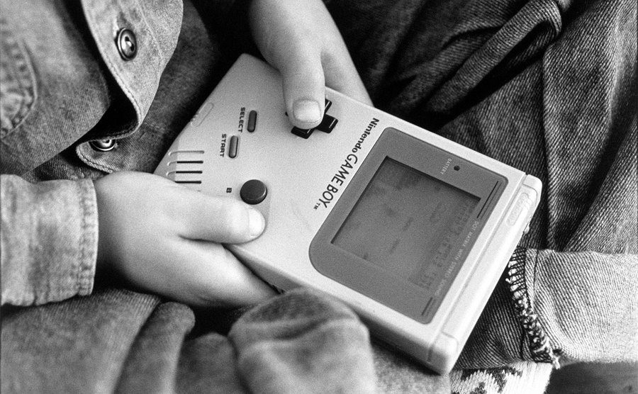 A boy is playing on one of the first Nintendo Game Boy computers. 
