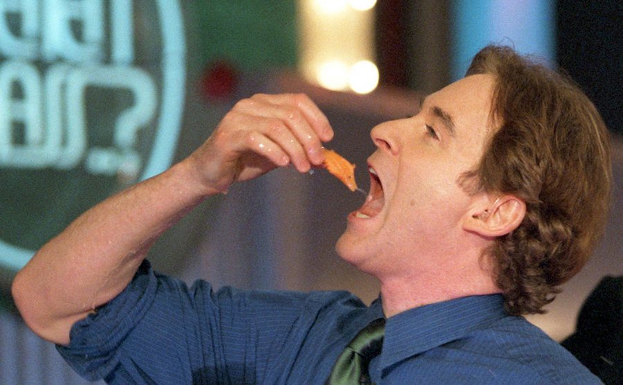 An image of Kevin Kline pretending to eat a raw fish on a live show.